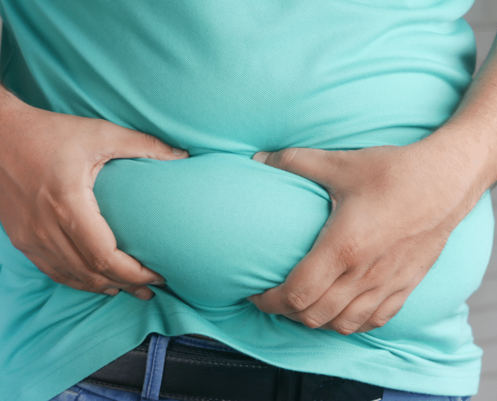 A person holding excess belly fat through their shirt, symbolizing obesity concerns and potential weight loss solutions—relevant to discussions on gastric sleeve cost.