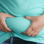 A person holding excess belly fat through their shirt, symbolizing obesity concerns and potential weight loss solutions—relevant to discussions on gastric sleeve cost.