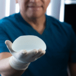 A surgeon in blue scrubs holding a silicone implant, representing the preparation process for breast augmentation surgery.