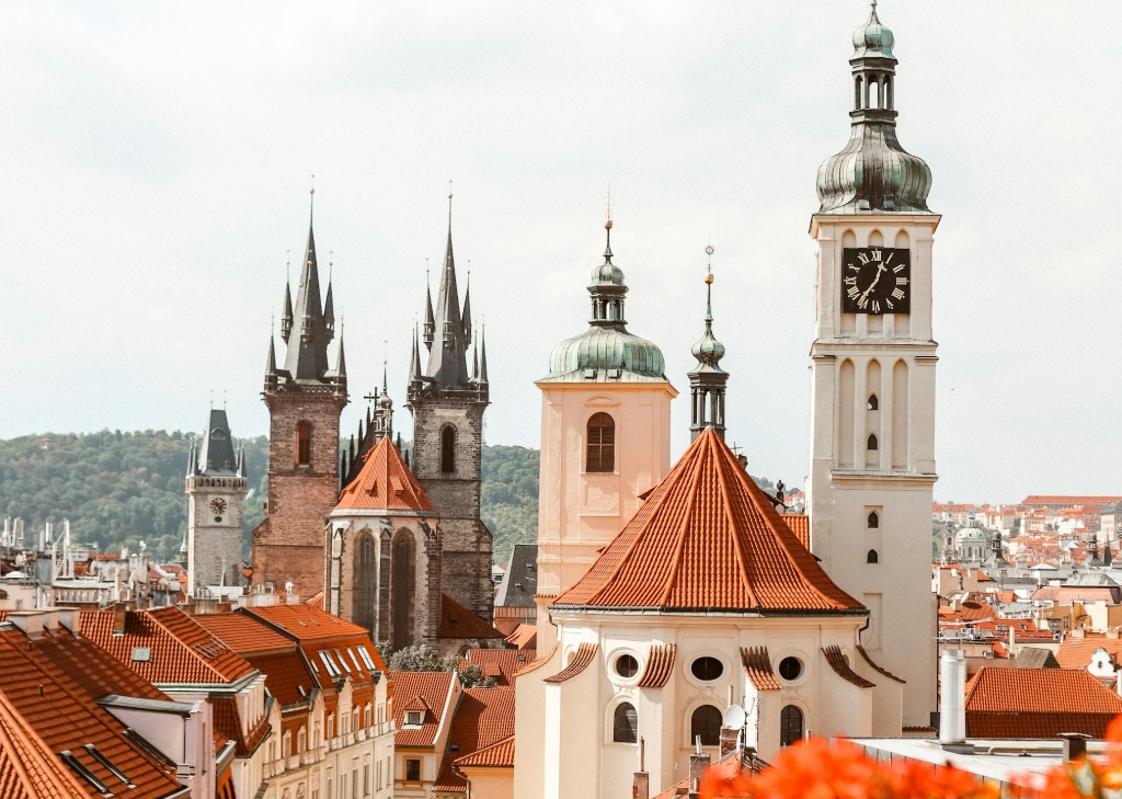 A scenic view of Prague's Old Town, featuring several historic buildings with distinctive red-tiled roofs and tall spires against a bright sky, often visited by those considering plastic surgery Prague.