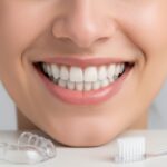 Close-up of a perfect, radiant smile with full porcelain teeth, subtly showing a nightguard and toothbrush for maintenance and care.